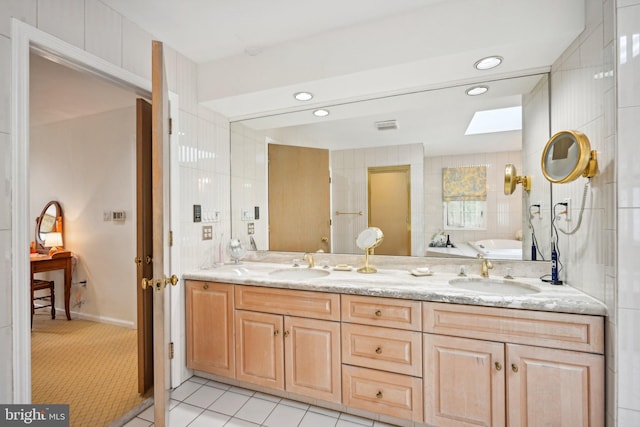 bathroom with tile patterned flooring, a skylight, a bath, and vanity