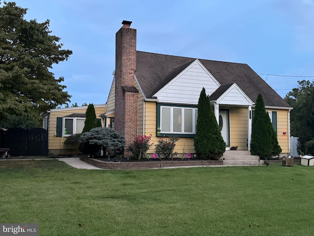 view of front facade featuring a shingled roof, a chimney, and a front yard