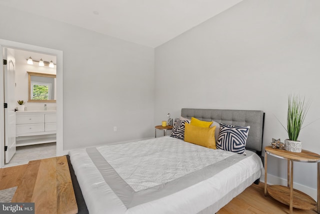 bedroom featuring light hardwood / wood-style flooring, connected bathroom, and lofted ceiling