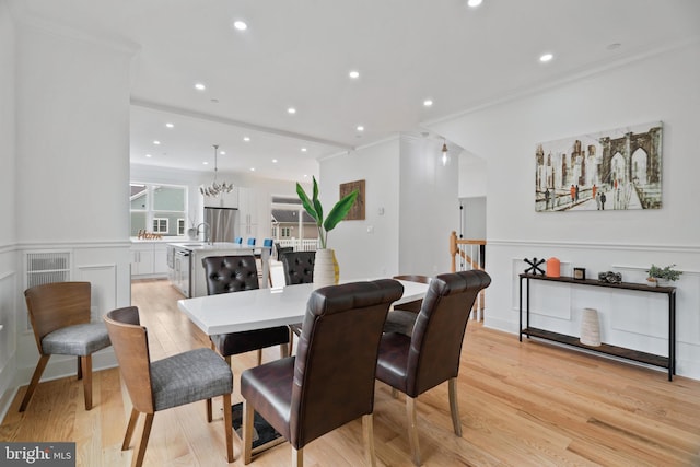 dining area with ornamental molding, sink, light hardwood / wood-style flooring, and a chandelier