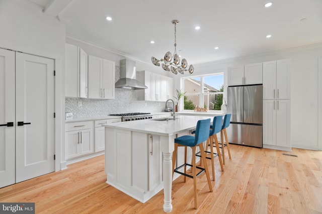 kitchen with a center island with sink, wall chimney exhaust hood, stainless steel appliances, and white cabinetry