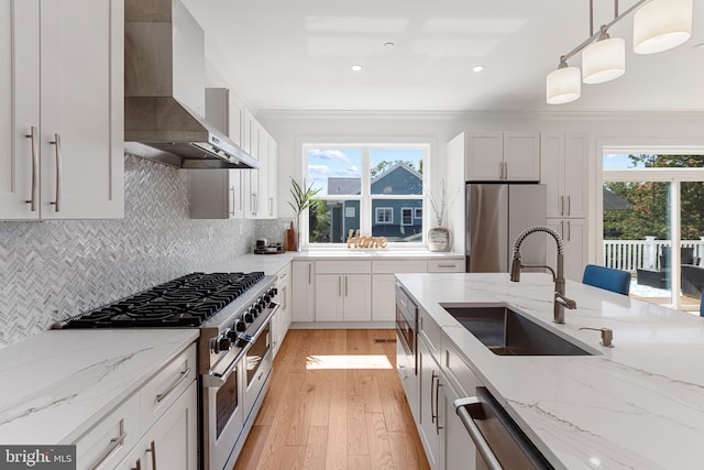 kitchen featuring appliances with stainless steel finishes, a healthy amount of sunlight, wall chimney exhaust hood, and decorative light fixtures