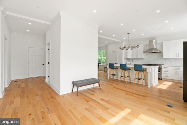 kitchen with white cabinets, a center island with sink, wall chimney exhaust hood, and light hardwood / wood-style flooring