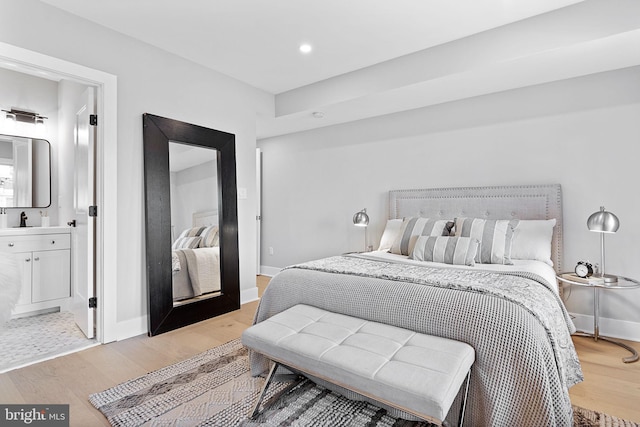 bedroom featuring light wood-type flooring, ensuite bathroom, and sink