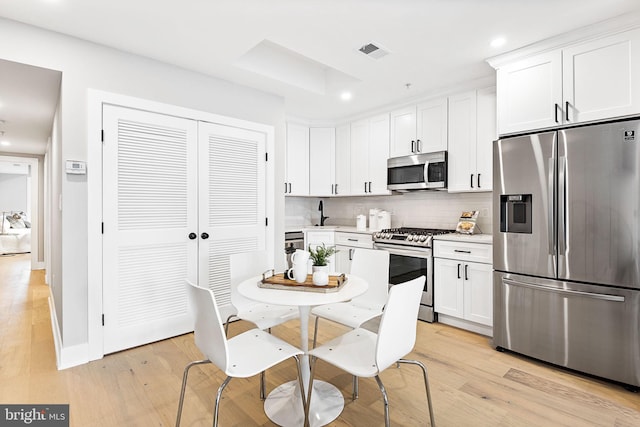 kitchen featuring light wood-type flooring, appliances with stainless steel finishes, decorative backsplash, and white cabinetry