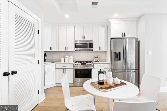 kitchen featuring light wood-type flooring, stainless steel appliances, white cabinetry, sink, and decorative backsplash