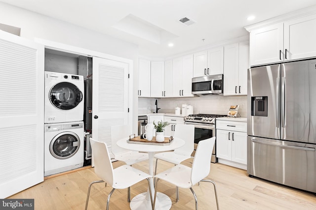 kitchen with light wood-type flooring, white cabinets, stainless steel appliances, and stacked washing maching and dryer