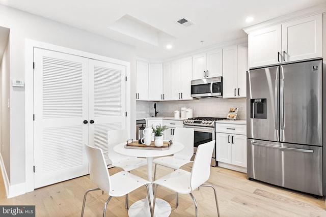 kitchen featuring appliances with stainless steel finishes, sink, decorative backsplash, white cabinetry, and light wood-type flooring