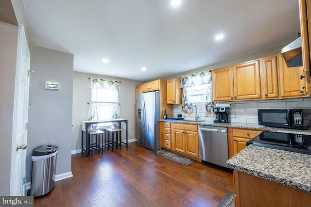 kitchen with tasteful backsplash, stainless steel appliances, light stone counters, sink, and dark wood-type flooring