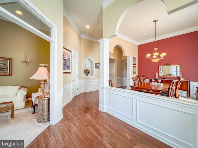 interior space with light wood-type flooring, decorative columns, an inviting chandelier, and ornamental molding