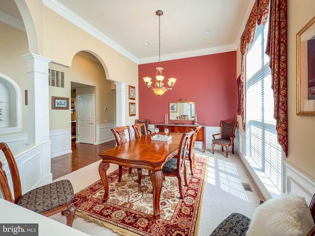 dining space with hardwood / wood-style floors, decorative columns, an inviting chandelier, and crown molding