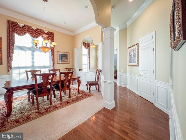 dining area featuring an inviting chandelier, ornamental molding, dark wood-type flooring, and decorative columns