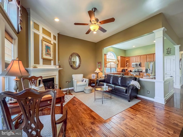 living room featuring decorative columns, ceiling fan, a large fireplace, and light wood-type flooring