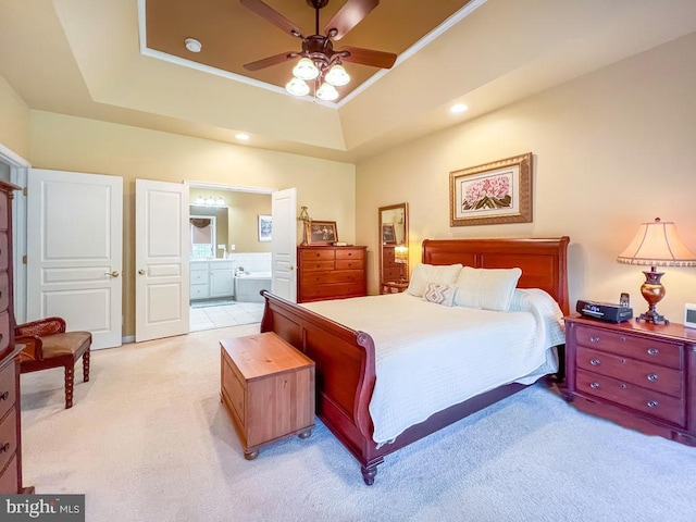 bedroom with a raised ceiling, ceiling fan, light colored carpet, and ensuite bathroom