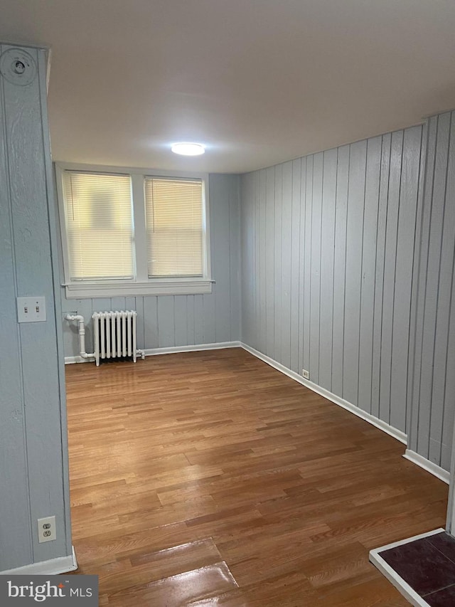 spare room with radiator, wooden walls, and light wood-type flooring