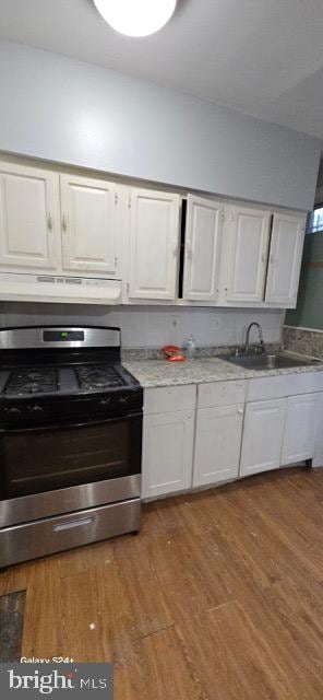 kitchen with range hood, stainless steel gas range, sink, hardwood / wood-style floors, and white cabinetry