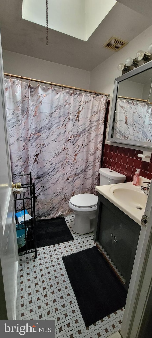 bathroom with tile patterned flooring, toilet, tile walls, tasteful backsplash, and vanity