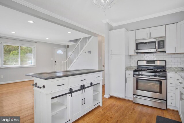 kitchen featuring backsplash, crown molding, light wood-type flooring, appliances with stainless steel finishes, and white cabinetry