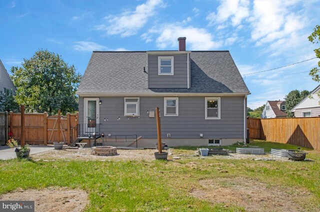 back of house with an outdoor fire pit and a yard