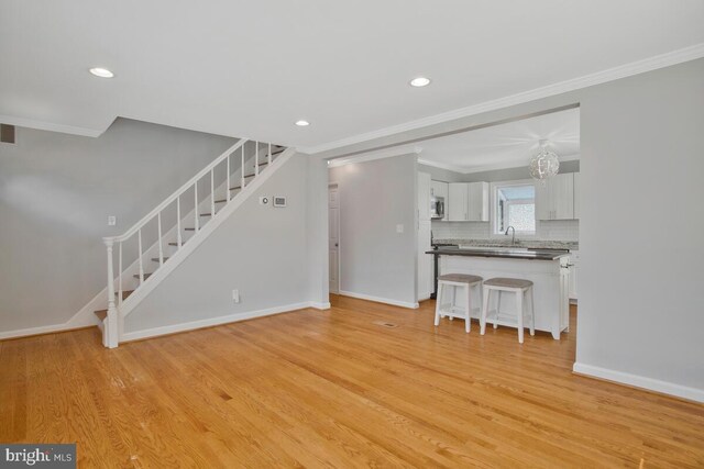 unfurnished living room with crown molding, sink, and light wood-type flooring