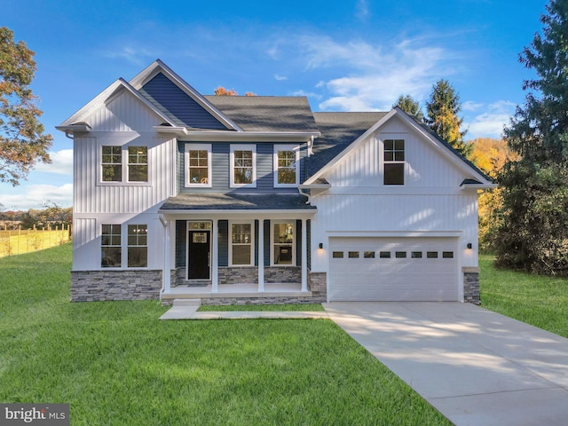 view of front facade with driveway, stone siding, covered porch, a front yard, and a shingled roof