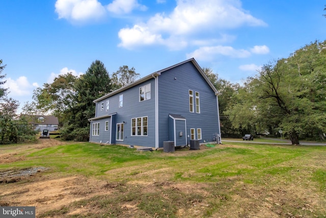 rear view of property with central air condition unit and a lawn