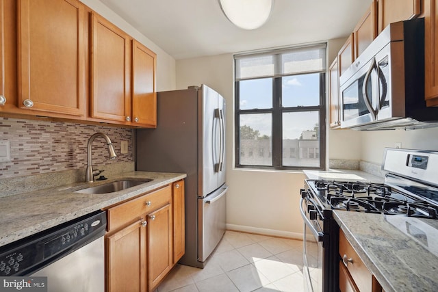 kitchen featuring backsplash, sink, light tile patterned floors, appliances with stainless steel finishes, and light stone counters