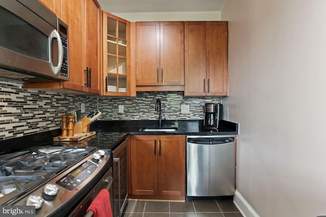 kitchen with appliances with stainless steel finishes, dark tile patterned floors, tasteful backsplash, and sink