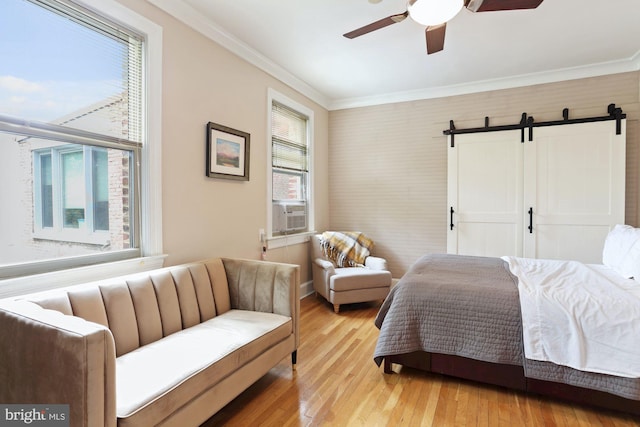 bedroom featuring light wood-type flooring, crown molding, ceiling fan, and a barn door