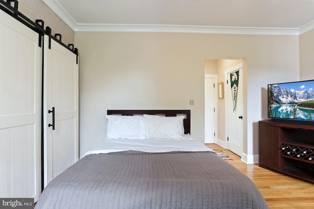 unfurnished bedroom with a barn door, crown molding, and light hardwood / wood-style flooring