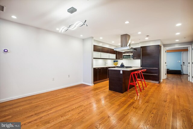 kitchen featuring a kitchen bar, island range hood, decorative light fixtures, and light wood-type flooring