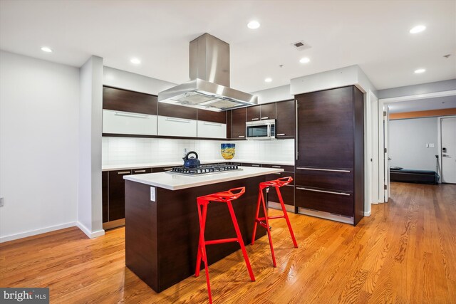 kitchen with a center island, stainless steel appliances, light hardwood / wood-style floors, island range hood, and a breakfast bar