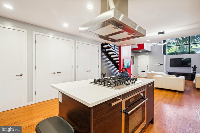 kitchen with appliances with stainless steel finishes, a kitchen island, island range hood, and light hardwood / wood-style flooring