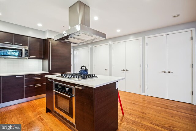 kitchen with ventilation hood, appliances with stainless steel finishes, a center island, and light hardwood / wood-style floors