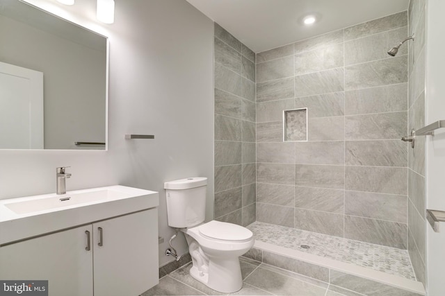 bathroom with tiled shower, vanity, toilet, and tile patterned flooring