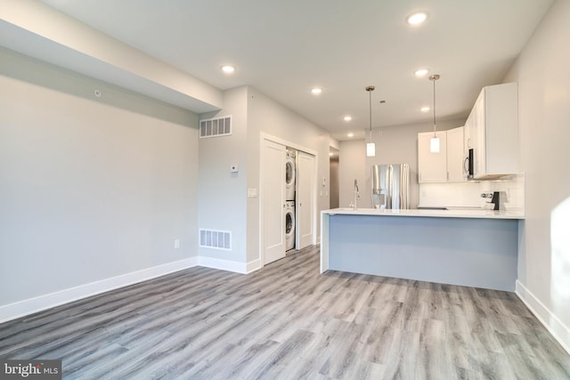 kitchen featuring light wood-type flooring, stacked washer / dryer, white cabinetry, kitchen peninsula, and appliances with stainless steel finishes