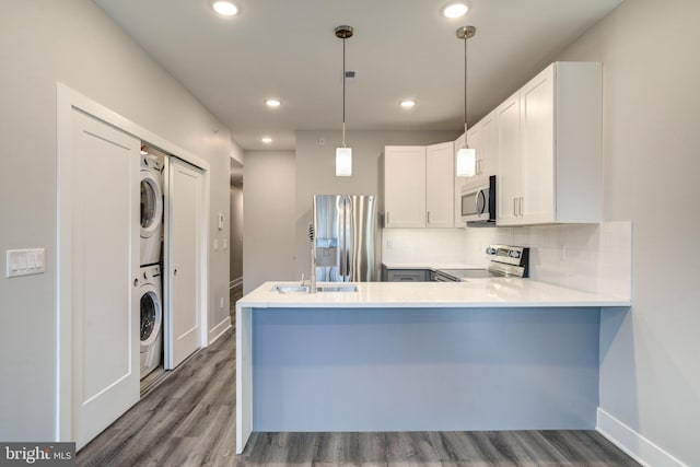 kitchen featuring stacked washer and dryer, white cabinets, kitchen peninsula, hanging light fixtures, and stainless steel appliances