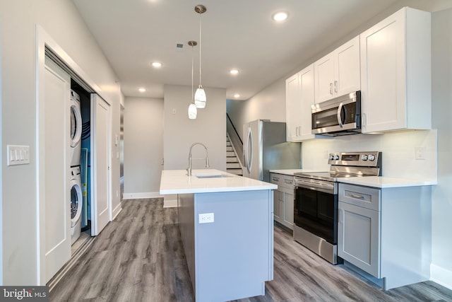 kitchen with stacked washer / drying machine, sink, an island with sink, hanging light fixtures, and stainless steel appliances