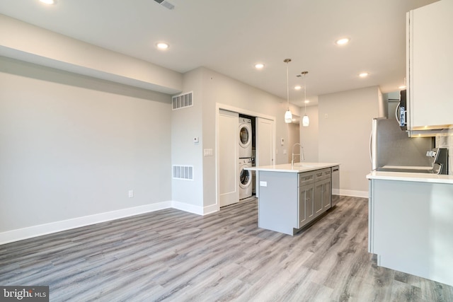 kitchen with stacked washer and dryer, light hardwood / wood-style flooring, decorative light fixtures, a center island with sink, and sink