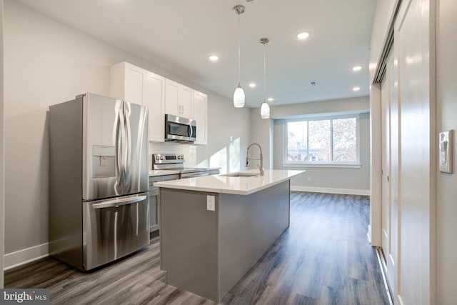 kitchen with appliances with stainless steel finishes, white cabinetry, decorative light fixtures, a center island with sink, and dark hardwood / wood-style floors