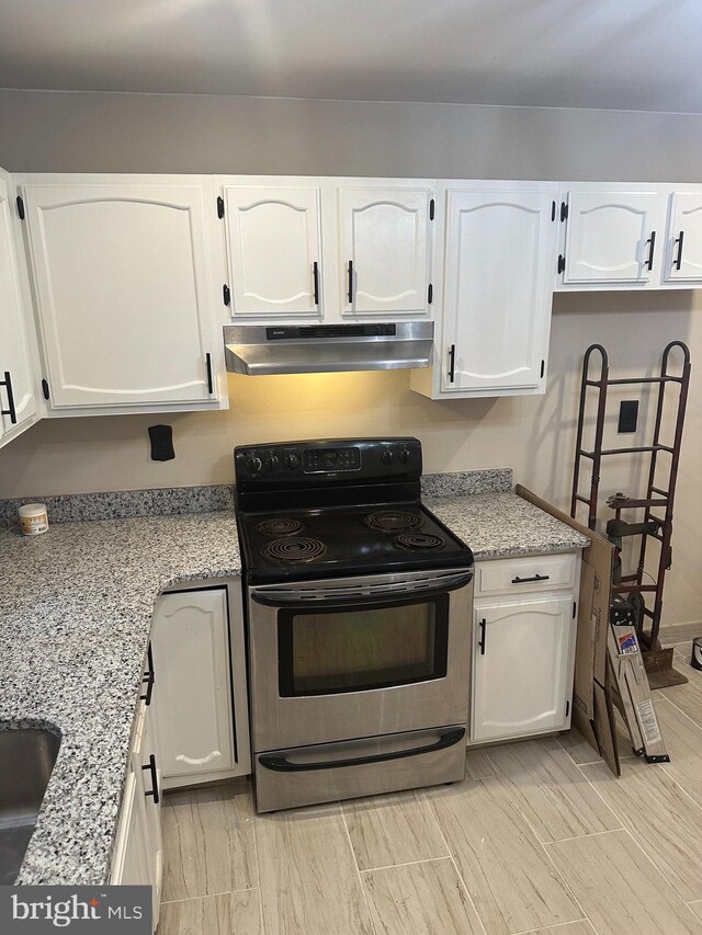 kitchen with light stone counters, electric stove, and white cabinetry