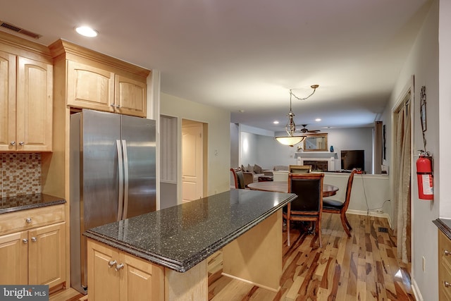 kitchen featuring light brown cabinetry, dark stone counters, stainless steel refrigerator, light hardwood / wood-style floors, and decorative light fixtures