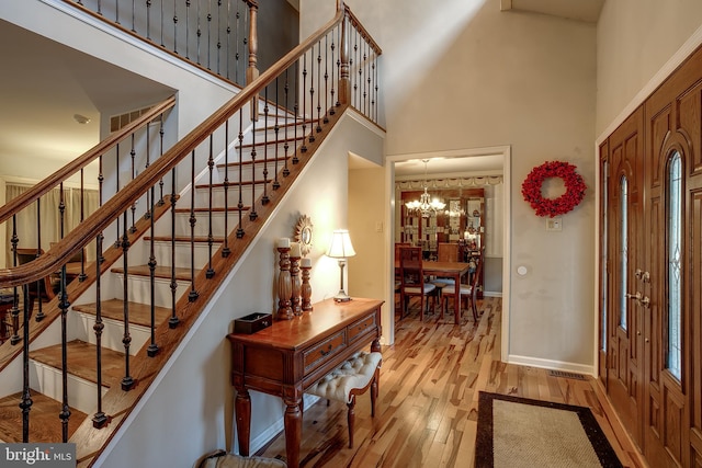 entryway featuring a towering ceiling, an inviting chandelier, and light wood-type flooring