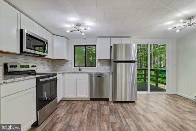 kitchen featuring hardwood / wood-style floors, white cabinets, sink, appliances with stainless steel finishes, and light stone counters