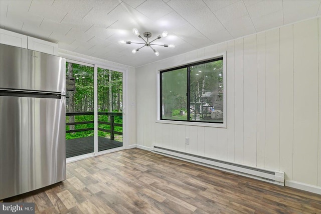 unfurnished room featuring baseboard heating, an inviting chandelier, a healthy amount of sunlight, and wood-type flooring