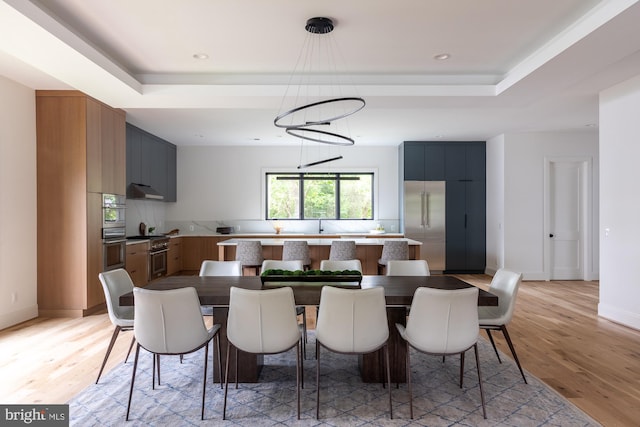 dining space with a tray ceiling, an inviting chandelier, and light hardwood / wood-style flooring