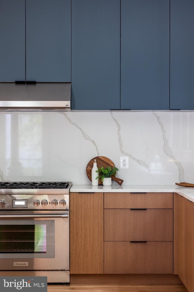 kitchen with range hood, light stone countertops, stainless steel range, blue cabinets, and tasteful backsplash