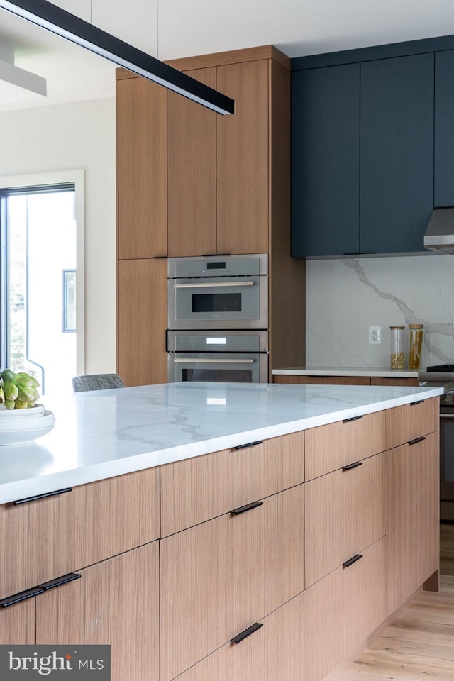 kitchen with light wood-type flooring, range hood, light stone countertops, decorative backsplash, and appliances with stainless steel finishes