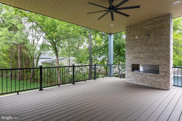 deck featuring an outdoor stone fireplace and ceiling fan