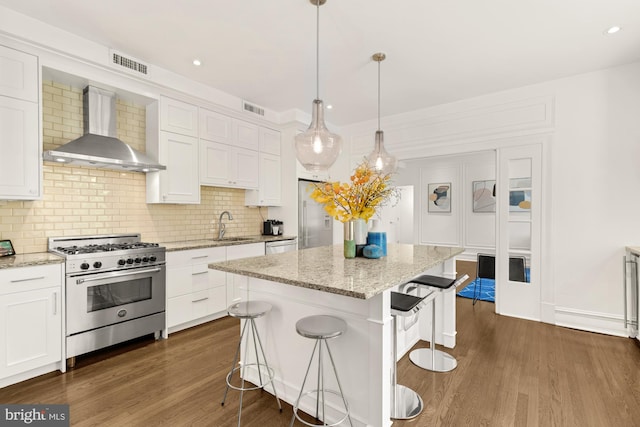 kitchen featuring stainless steel appliances, dark hardwood / wood-style floors, wall chimney range hood, and white cabinetry